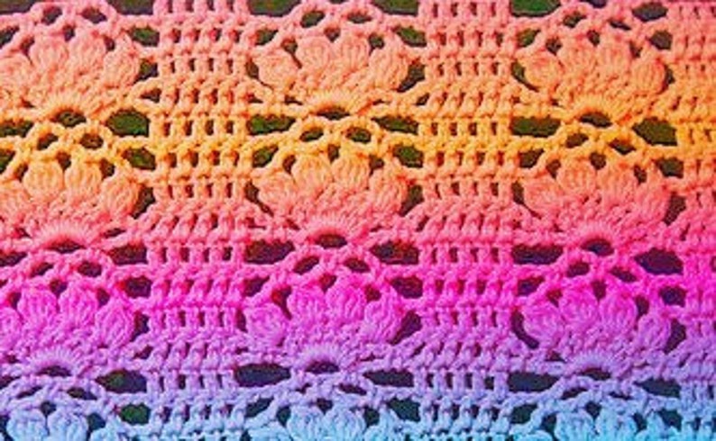 May include: A close-up of a colourful crochet fabric with a repeating pattern of flowers. The fabric is made with a gradient of colours, starting with blue and transitioning to pink, orange, and yellow.