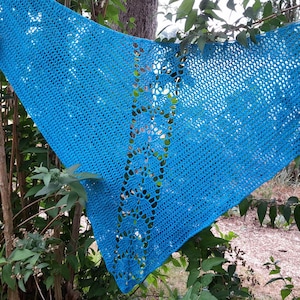 Puede incluir: Un chal triangular de color azul brillante que presenta un intrincado patrón de ganchillo con una columna vertical central de motivos calados en forma de hoja, flanqueada por secciones de punto de red repetitivo en toda la prenda.