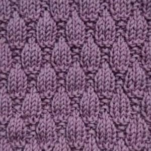 Könnte beinhalten: Eine Nahaufnahme eines gestrickten Stoffes mit einem strukturierten Muster. Der Stoff ist helllila und hat ein sich wiederholendes Muster aus kleinen, abgerundeten Formen.