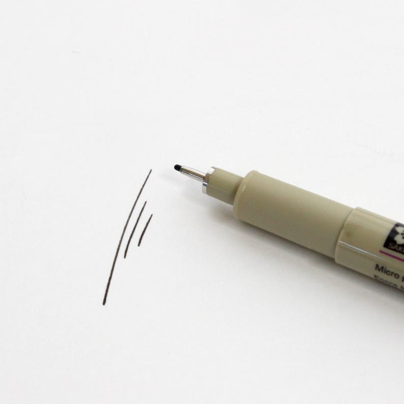 Op de afbeelding: Een zwarte fijnlijnstift met een beige cilinder en de tekst "Sakura Micro Pen" gedrukt op de zijkant.