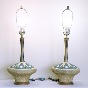 May include: A pair of mid-century modern table lamps with a ceramic base and a wood-toned stem. The bases are textured and feature a geometric design in shades of white, blue, and green.