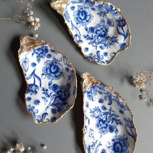 Könnte beinhalten: Drei Austernmuscheln, die mit einem blauen und weißen Blumenmuster bemalt sind. Die Ränder der Muscheln sind golden bemalt.