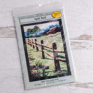 May include: A quilting pattern for a split rail fence with a farmhouse in the background. The pattern is printed on white paper with a blue border and the title "Split Rail" in black text.