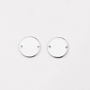 以下が含まれることがあります： 2つの穴がそれぞれ開いた、銀色の丸い金属製のチャームが2つ。チャームは空白で、パーソナライズする準備ができています。