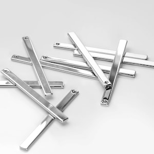 May include: A group of silver metal bars with rounded ends. The bars are arranged in a random pattern on a white surface.