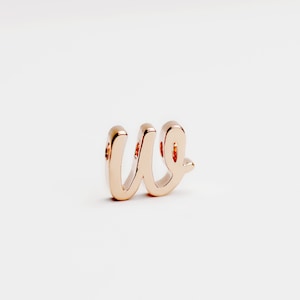 May include: A gold-coloured metal charm in the shape of the letter "w" with a cursive font.