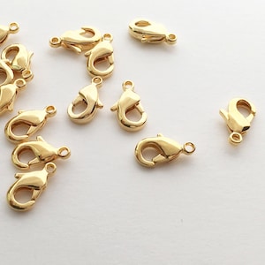 May include: A group of 12 gold-tone metal lobster claw clasps. The clasps are small and have a shiny finish.