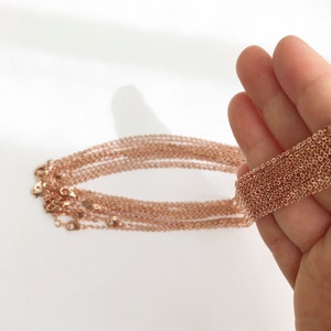 May include: A stack of rose gold chain necklaces with lobster claw clasps. The chains are delicate and have a fine, smooth texture.