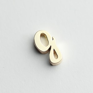 May include: A gold-colored letter G charm, in a cursive script style.