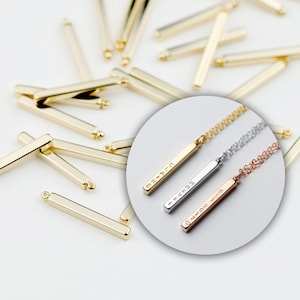 May include: Three gold bar pendants with different inscriptions on them. The pendants are on chains and are hanging from a white background. The inscriptions on the pendants are "MR-ATO", "I-AXTR", and "Q-MON-4VM".