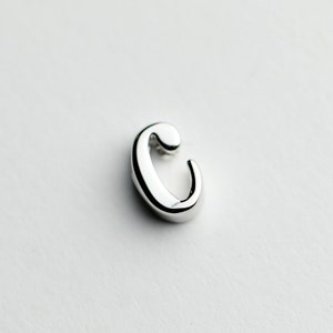 May include: A silver charm in the shape of the letter C.