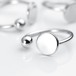May include: A silver ring with a large, round, smooth, white disc and a small silver ball on the side.