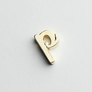May include: Gold-colored metal letter 'p' charm. The letter is in a cursive style.