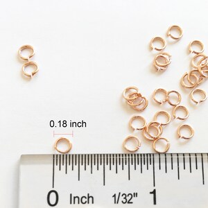 May include: A close-up of a ruler measuring a small gold jump ring. The ring is 0.18 inches in diameter. There are many other jump rings scattered around the ruler.