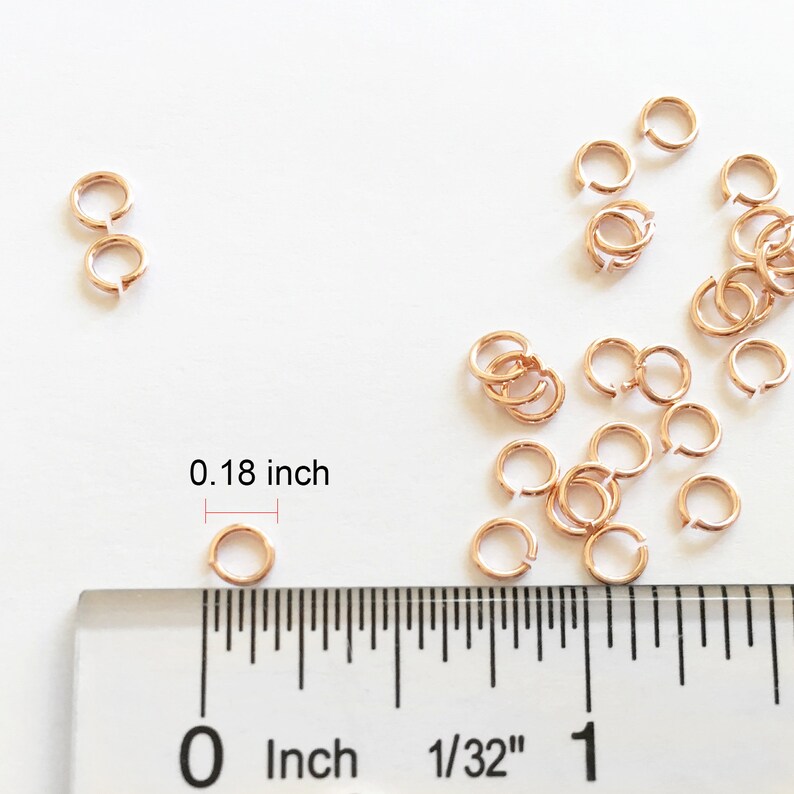 May include: A close-up of a ruler measuring a small gold jump ring. The ring is 0.18 inches in diameter. There are many other jump rings scattered around the ruler.