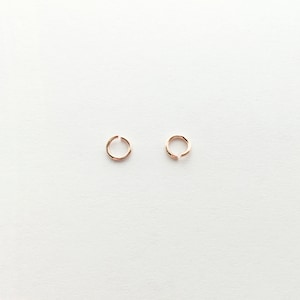 May include: Two small, gold-colored hoop earrings. The hoops are simple and delicate, with a smooth finish.