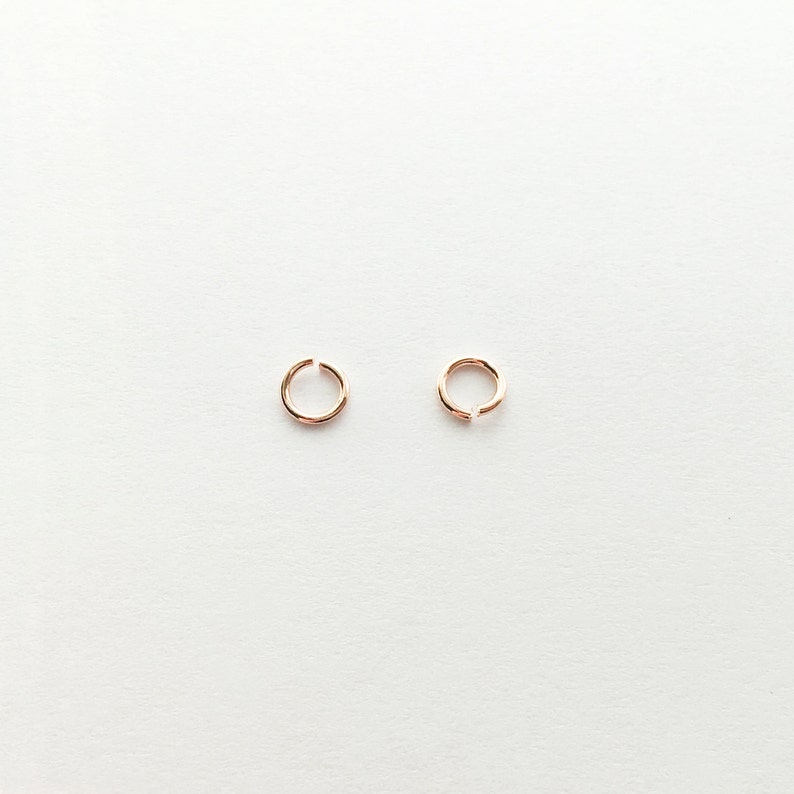 May include: Two small, gold-colored hoop earrings. The hoops are simple and delicate, with a smooth finish.