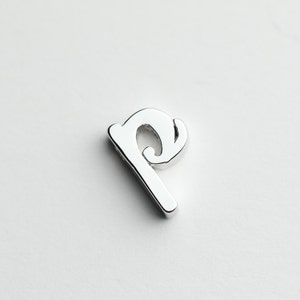 May include: A silver charm in the shape of the letter 'p'. The letter is stylized with a decorative flourish.