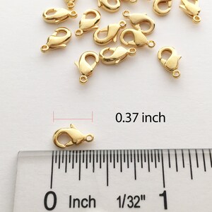 May include: Gold-toned metal lobster clasps, measuring 0.37 inches in length, scattered on a white surface next to a ruler.