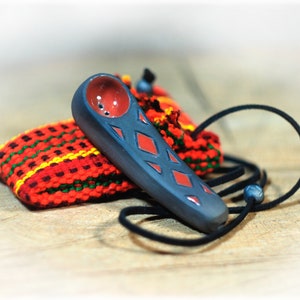 May include: A small, black ceramic pipe with red diamond-shaped designs. The pipe has a small bowl and a long, narrow stem. It is hanging from a black cord with a bead.