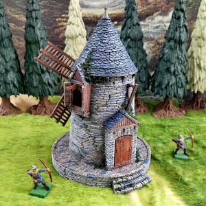 May include: A miniature stone windmill with a blue-gray tiled roof and wooden accents. The windmill has a round base and a small wooden door. Two miniature archers stand nearby on a green surface, with a backdrop of miniature trees.