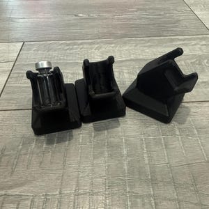 Könnte beinhalten: Drei schwarze, 3D-gedruckte Ständer. Ein Ständer hält eine kleine, klare Glasflasche mit silbernem Deckel. Die anderen beiden Ständer sind leer. Die Ständer stehen auf einer grauen Holzoberfläche. Die Ständer scheinen für kleine Objekte konzipiert zu sein.