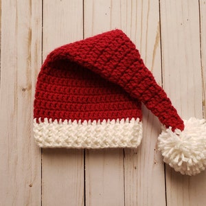 May include: A red and white crocheted Santa hat with a white pom-pom on the end.