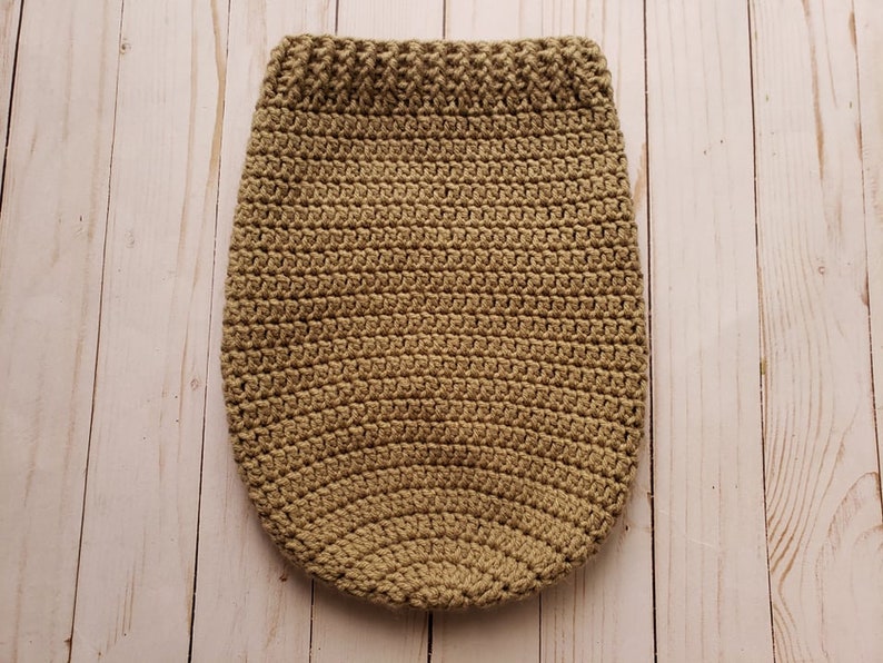 May include: A crocheted beige baby sleeping bag with a textured pattern.