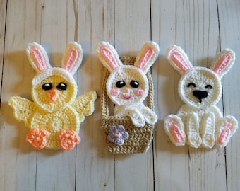 May include: Three crocheted Easter decorations: a yellow chick wearing bunny ears, a white bunny in a basket, and a white bunny sitting.