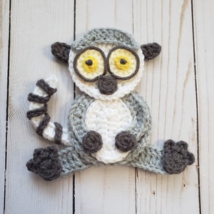 May include: A crocheted lemur toy with white and gray yarn. The lemur has yellow eyes and a black nose.