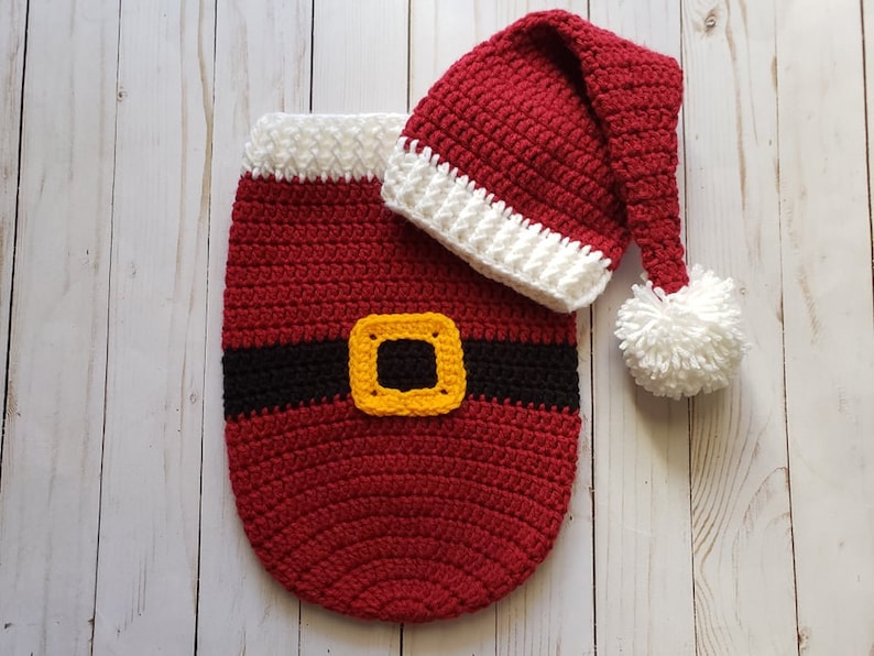 May include: Red and white crocheted Santa hat and a red crocheted Santa outfit with a black belt and a yellow buckle.
