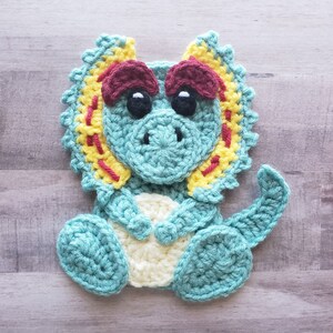 May include: A crocheted triceratops dinosaur toy with a teal body, yellow and red frill, and white eyes.