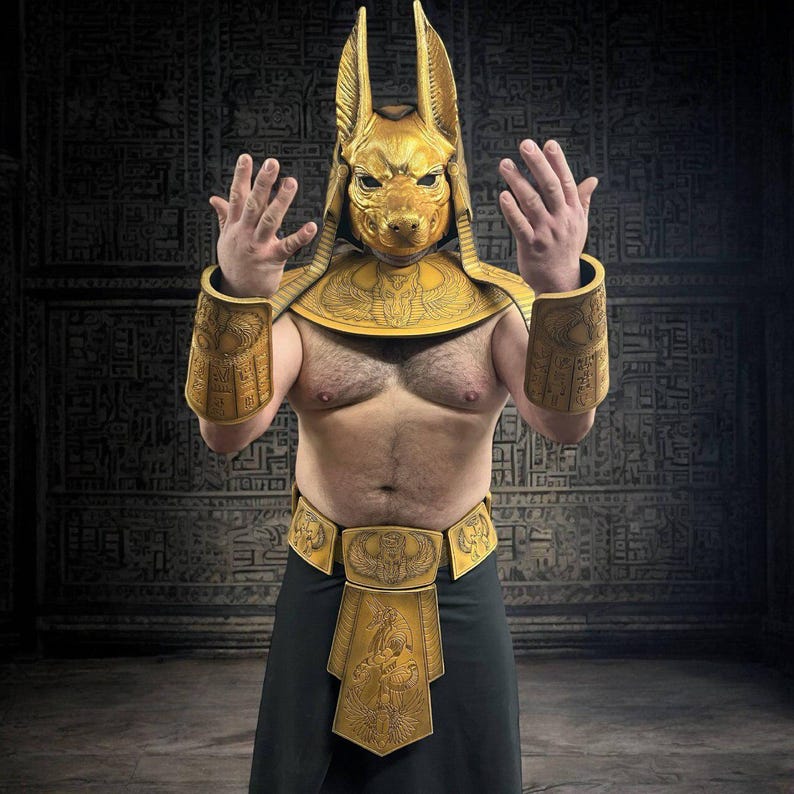 May include: A person wearing a gold Anubis costume with a mask, a collar, arm guards, and a belt. The costume is decorated with hieroglyphics.