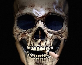 May include: A white skull mask with a cigarette in its mouth. The mask has a realistic appearance with detailed features, including teeth and eye sockets.