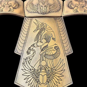 May include: A gold-colored metal necklace with an Egyptian theme. The necklace features a central pendant with a winged scarab beetle, a standing Anubis figure, and two smaller pendants with seated jackals. The necklace is decorated with intricate line drawings.