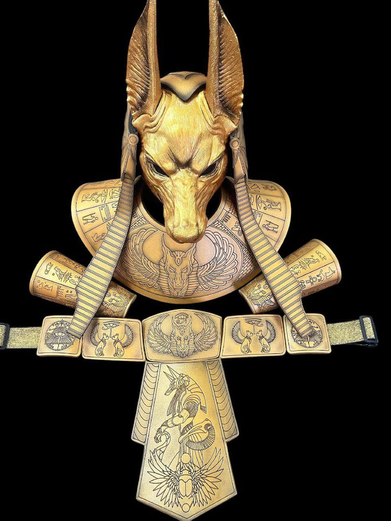 May include: A gold-colored Anubis costume set with a mask, collar, and belt. The mask features a jackal head with intricate details. The collar and belt are adorned with Egyptian hieroglyphs and winged scarabs.