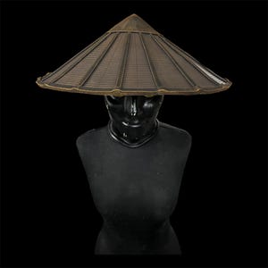 以下が含まれることがあります： 黒いマネキンに展示された、ブロンズ色の幅広のつばが付いたアジアの円錐形の帽子。帽子はスラットデザインと尖った上部を備えています。マネキンは黒色で、滑らかで反射する表面を持っています。背景は無地です。