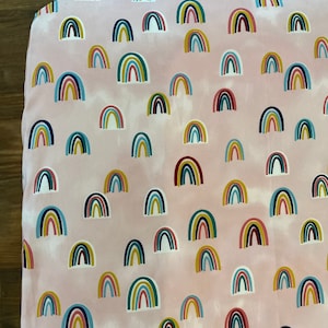 May include: Pink fitted sheet with a repeating pattern of colorful rainbows. The sheet is made of soft, breathable fabric and is perfect for a crib or toddler bed.