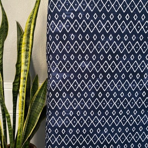 Pu&ograve; includere: Un tessuto blu navy con un motivo geometrico a rombi bianchi. Il tessuto ha un aspetto leggermente strutturato.