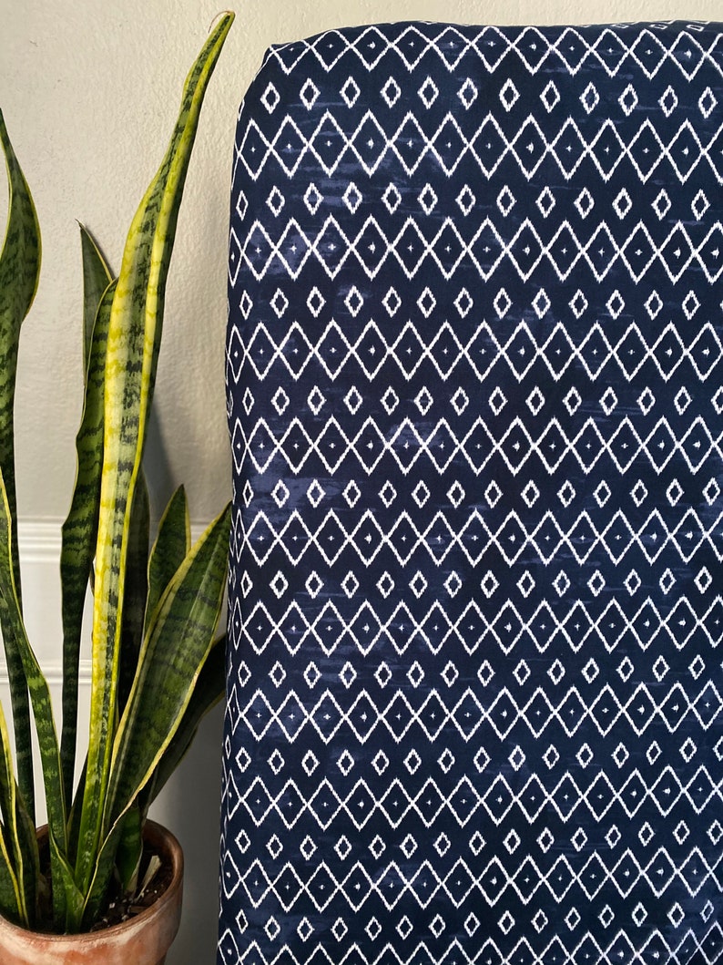 Pu&ograve; includere: Un tessuto blu navy con un motivo geometrico a rombi bianchi. Il tessuto ha un aspetto leggermente strutturato.