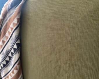 May include: A soft, green, textured fabric with a woven pattern. The fabric is folded and draped over a surface.