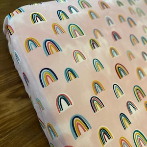 May include: Pink fitted crib sheet with a repeating pattern of colorful rainbows.