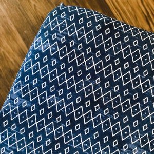 Pu&ograve; includere: Primo piano di un tessuto blu con un motivo geometrico bianco. Il tessuto ha un motivo a rombi con linee bianche.