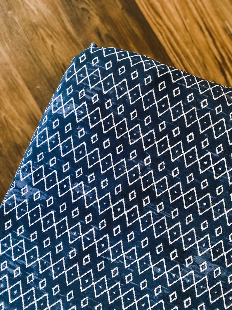 Pu&ograve; includere: Primo piano di un tessuto blu con un motivo geometrico bianco. Il tessuto ha un motivo a rombi con linee bianche.
