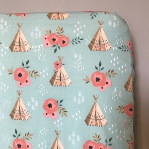 May include: A turquoise blue fitted sheet with a repeating pattern of pink flowers, brown teepees, and white geometric shapes.