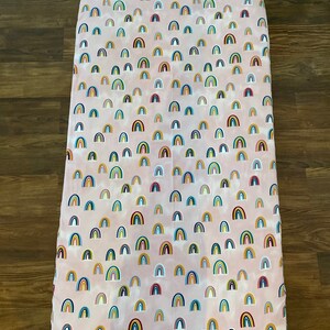 May include: Pink fitted crib sheet with a repeating pattern of colorful rainbows.