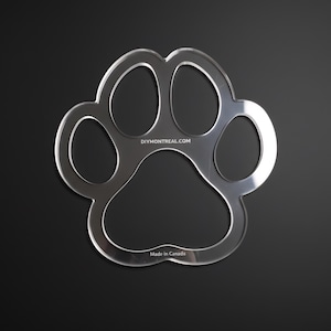 May include: Clear acrylic paw print stencil with rounded edges, set against a black background. The stencil features five distinct toe pads and the text "DIYMONTREAL.COM" and "Made in Canada".