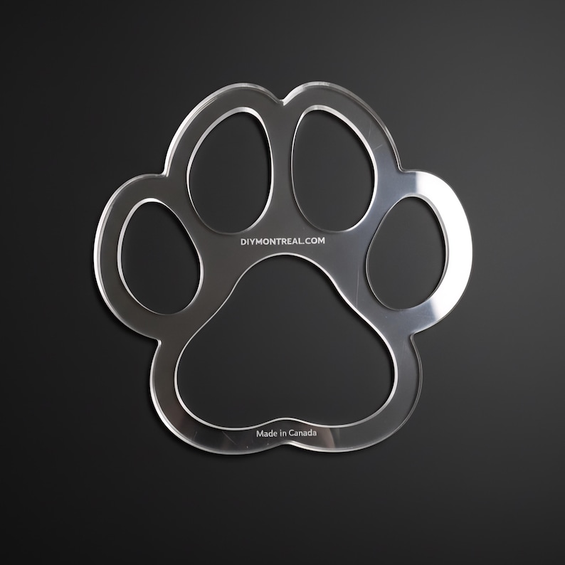 May include: Clear acrylic paw print stencil with rounded edges, set against a black background. The stencil features five distinct toe pads and the text "DIYMONTREAL.COM" and "Made in Canada".