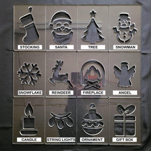 May include: A set of clear acrylic Christmas stencils featuring festive designs. Includes a stocking, Santa, tree, snowman, snowflake, reindeer, fireplace, angel, candle, string lights, ornament, and gift box. Each stencil has the design's name printed below.