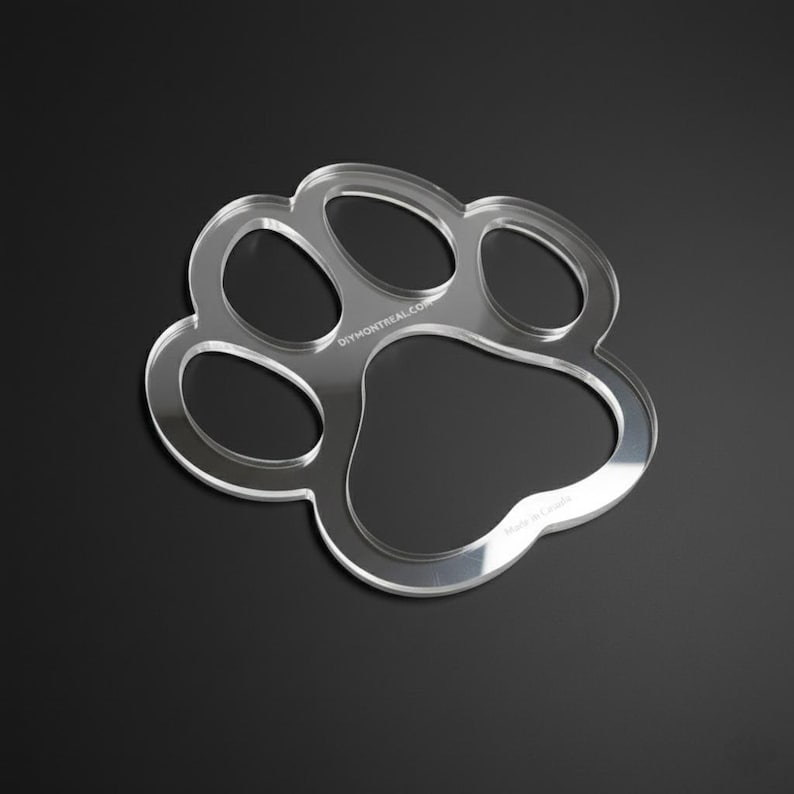 May include: Clear acrylic paw print shape with rounded edges, designed with five distinct sections. The text "DIYMONTREAL.COM" is visible on the top left, and "Made in Canada" is on the bottom right. The object is on a black background.